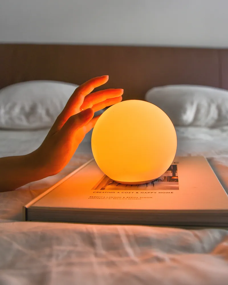 A hand reaching towards an amber SensoLight on a book by the bed