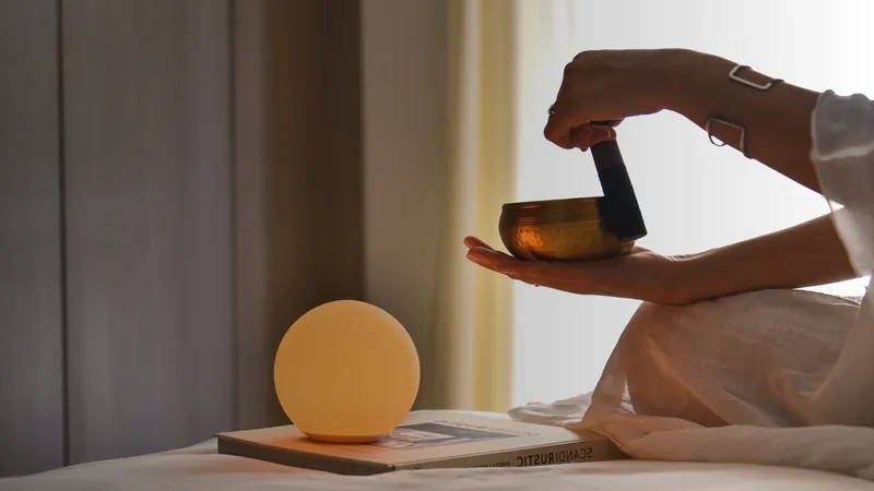 A warm SensoLight on a bedside table, with a hand holding a singing bowl